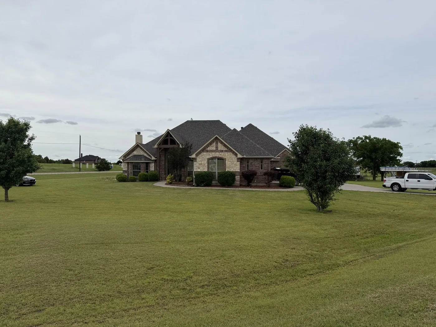 Large brick and stone custom home with dark shingle roof on a spacious lot